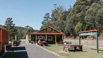 A wooden building with a red roof, labeled 'Noojee Heritage,' with picnic tables and a signboard.