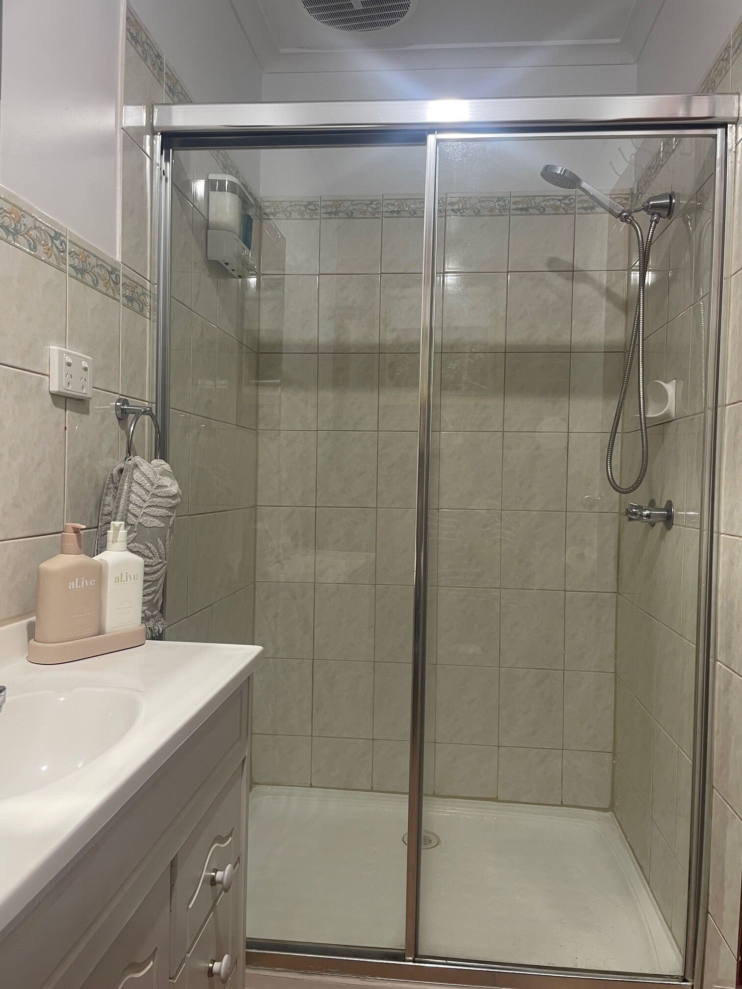 A shower with a glass door, a towel hanging on a rack, and toiletries on the sink.
