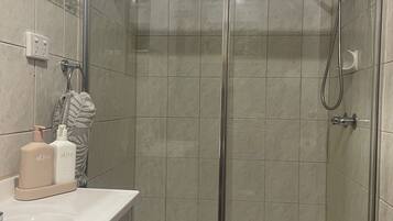 A shower with a glass door, a towel hanging on a rack, and toiletries on the sink.