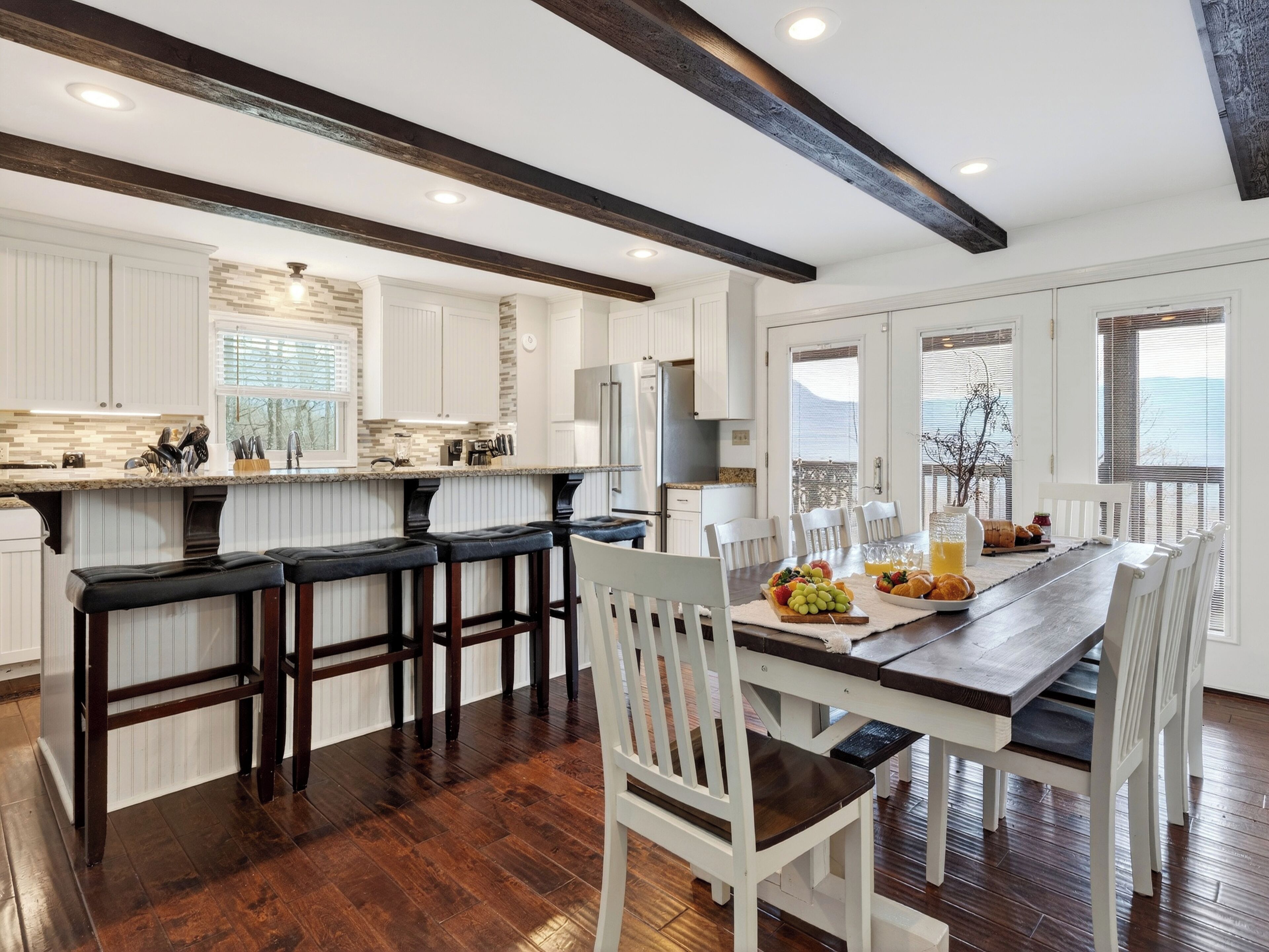 A modern kitchen with white cabinetry, dark wooden beams, and a breakfast bar.
