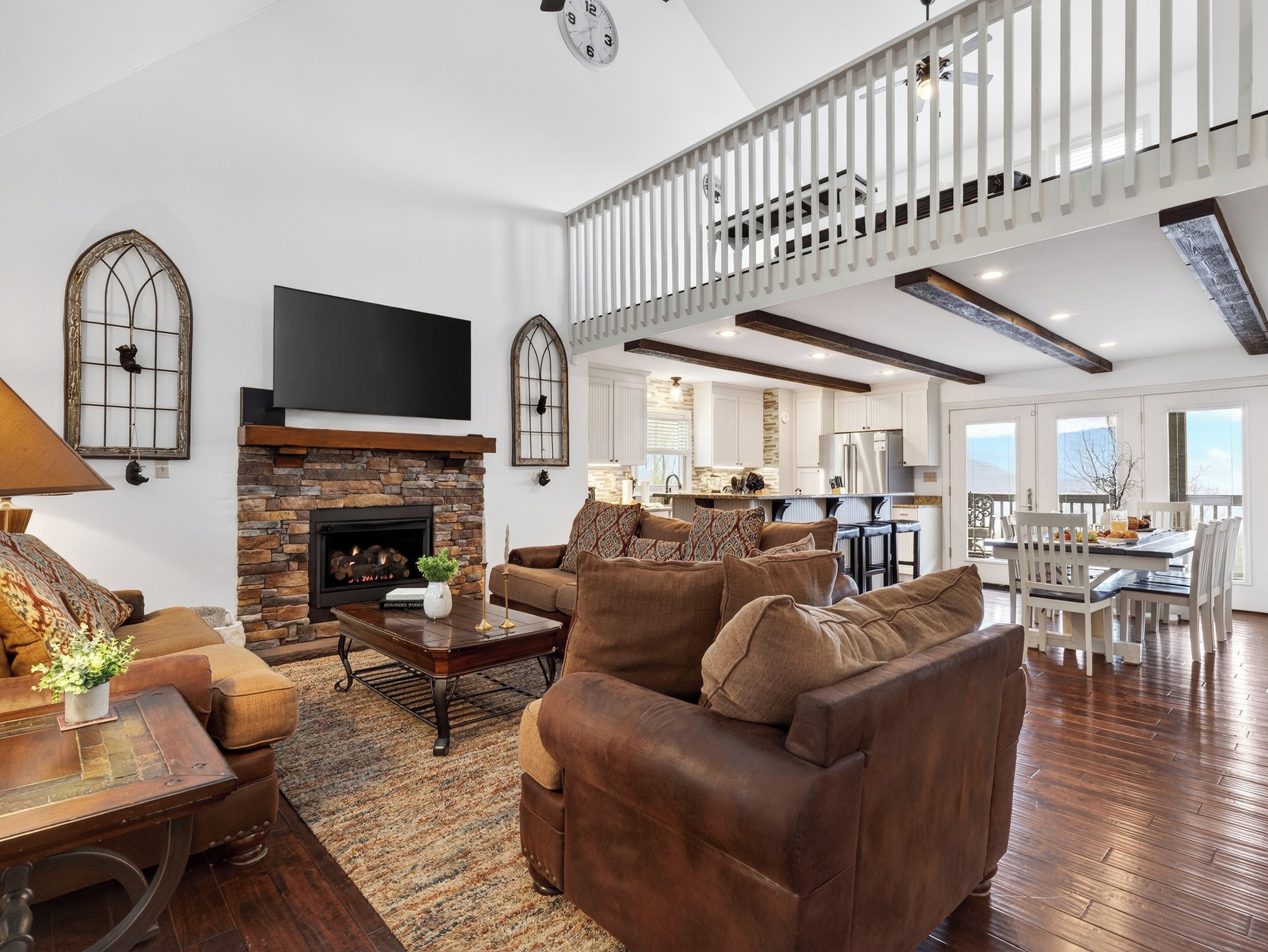 Spacious living room with a stone fireplace, leather seating, and a loft overlook.