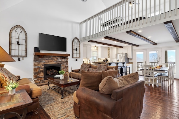 Spacious living room with a stone fireplace, leather seating, and a loft overlook.