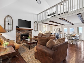 A spacious living room with a fireplace, leather sofas, a flat-screen TV, and a kitchen in the background. - Gatlinburg Cabin • Pool Table • Pool • Hot Tub • Sleeps 10 | Cobbly Nob Hideaway (Gatlinburg)