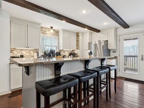 A kitchen with white cabinets, a granite countertop, a stainless steel refrigerator, and a bar area with stools. - Gatlinburg Cabin • Pool Table • Pool • Hot Tub • Sleeps 10 | Cobbly Nob Hideaway (Gatlinburg)