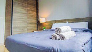Een hotelkamer met een groot bed, een nachtkastje met een lamp en een raam met jaloezieën.