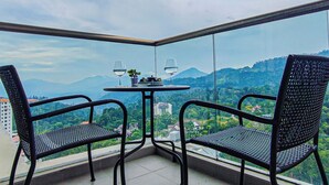 Een hoekbalkon met twee stoelen en een tafel, met uitzicht op bergen en een gebouw in de verte.