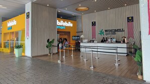 Een receptie met een balie, een bord met 'Windmill' erop en een 'Bilabila Mart' winkel op de achtergrond.