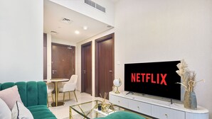 Uma sala de estar moderna com um sofá verde, uma mesa de centro branca, uma TV exibindo 'NETFLIX' e um console branco.