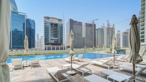Uma área de piscina no terraço com espreguiçadeiras e guarda-sóis, com vista para um horizonte urbano com edifícios modernos.