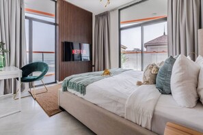 A modern hotel room with a large bed, a desk, a TV, and a view of the city. - Binghatti Avenue - 2407 (Dubai)