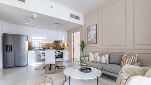 Un salon moderne avec un canapé, une table basse et un coin repas comprenant des chaises, et une cuisine en arrière-plan.