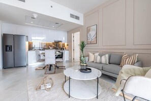 A modern living room with a sofa, a coffee table, and a dining area with chairs and a kitchen in the background. - Binghatti Avenue - 2407 (Dubai)