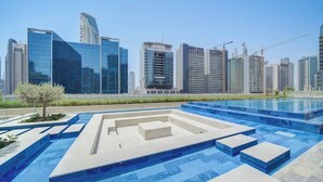 A modern swimming pool with geometric patterns, surrounded by high-rise buildings and construction cranes. - Vera Residence - 1303 (Dubai)