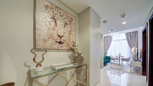 A modern interior with a glass console table, a large abstract painting, and a well-lit living area with a sofa and chairs. - Vera Residence - 1303 (Dubai)