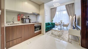 A modern kitchen with a built-in oven, a dining area with a glass table, and a green sofa. - Vera Residence - 1303 (Dubai)