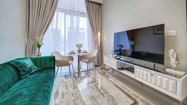 A modern living room with a green sofa, a TV on a white console, a dining table with chairs, and large windows with curtains. - Vera Residence - 1303 (Dubai)