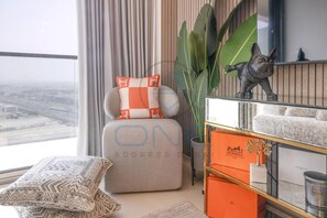 Ein stilvolles Wohnzimmer mit Blick auf eine Stadtlandschaft, eine Couch mit gemusterten Kissen, eine dekorative Hundestatue, eine große Pflanze und eine Vitrine mit Markenartikeln.