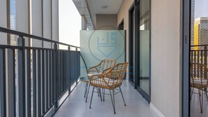 Un balcon avec deux fauteuils en osier, une porte vitrée et une vue sur de hauts immeubles.
