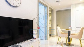 Un salon moderne doté d’un téléviseur à écran plat, d’un coin repas avec une table ronde et des chaises, et d’une porte visible donnant sur une autre pièce.