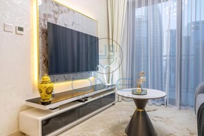 A modern living room with a flat-screen TV, a white console table, a round coffee table, and a large window with sheer curtains. - Designer Apartment in Zada Tower, Downtown (Dubai)