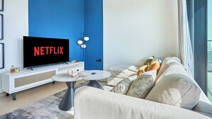 A modern living room with a large flat-screen TV, a white sofa, a coffee table, and a blue accent wall. - Binghatti Corner - 1508 (Dubai)