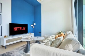 A modern living room with a large flat-screen TV, a white sofa, a coffee table, and a blue accent wall. - Binghatti Corner - 1508 (Dubai)