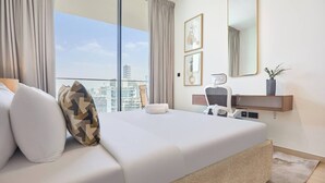A modern hotel room with a large bed, a desk, a chair, a mirror, and a view of the cityscape. - Binghatti Corner - 1508 (Dubai)