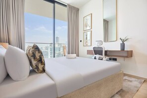 A modern hotel room with a large bed, a desk, a chair, a mirror, and a view of the cityscape. - Binghatti Corner - 1508 (Dubai)