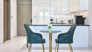 Eine moderne Küche mit zwei sesselförmigen Hocker in Türkis, einem Glastisch und einem kleinen Blumentopf.