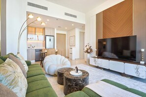Ein modernes Wohnzimmer mit einem großen Flachbildfernseher, einem grünen Sofa, einem weißen Sessel und einem Couchtisch aus Marmor.