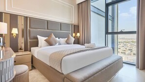 Et moderne hotelværelse med en stor seng, sengeborde, lamper, et rundt siddeområde og et stort vindue med udsigt over byen.