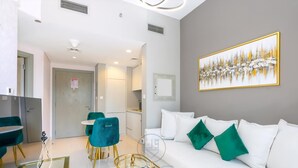 A modern living room with a white sofa, teal chairs, and a glass coffee table. - Zada Tower | 1BR, Big Balcony, Bright & Breezy (Dubai)