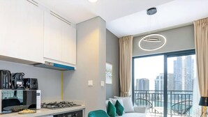 A modern kitchen with a gas stove, microwave, and coffee maker, a dining area with a table and chairs, and a balcony with a view of high-rise buildings. - Zada Tower | 1BR, Big Balcony, Bright & Breezy (Dubai)