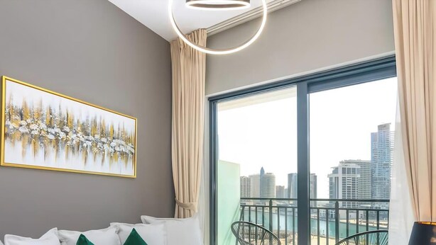A modern room with a city view, a framed artwork on the wall, and a balcony with a chair. - Zada Tower | 1BR, Big Balcony, Bright & Breezy (Dubai)