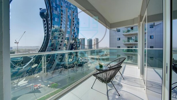 A modern balcony with a glass railing, a chair, and a view of a unique building and other high-rise structures. - Vera Residence - 814 (Dubai)