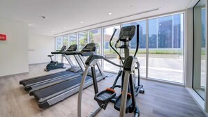 A gym with treadmills, ellipticals, and a red fire alarm. - Vera Residence - 814 (Dubai)