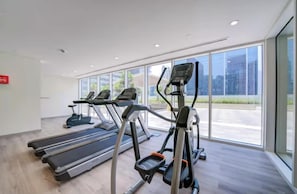 A gym with treadmills, ellipticals, and a red fire alarm. - Vera Residence - 814 (Dubai)