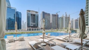 A rooftop pool area with lounge chairs and umbrellas, surrounded by high-rise buildings. - Vera Residence - 814 (Dubai)