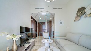 A modern living room with a flat-screen TV, a sofa, a coffee table, and a decorative vase. - Vera Residence - 814 (Dubai)