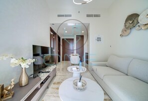 A modern living room with a flat-screen TV, a sofa, a coffee table, and a decorative vase. - Vera Residence - 814 (Dubai)