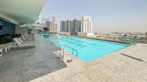 En pool på taget med liggestole, fri udsigt til skyskrabere og et fliset gulv.