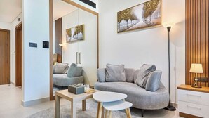 En moderne stue med en grå sofa, et lille rundt bord, et spejl og et billede på væggen.