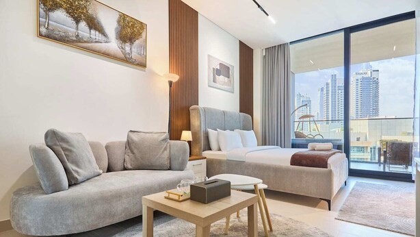 Et moderne hotelværelse med sofa, seng, lille bord og stort vindue med udsigt over byen.