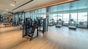Et moderne fitnesscenter med forskellig træningsudstyr, store vinduer og udsigt til bybilledet.