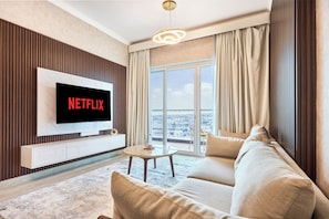Una sala moderna con una televisión de pantalla plana, un sofá, una mesa de centro y vistas de la ciudad a través de amplias ventanas.