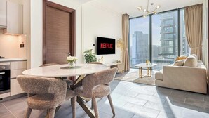 A modern living room with a dining area, a flat-screen TV, and a large window with a city view. - The Crest C Luxury Retreat | Stylish & Serene (Dubai)