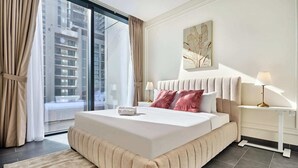 A modern hotel room with a large bed, a view of the city through floor-to-ceiling windows, a bedside table with a lamp, and a wall-mounted artwork. - The Crest C Luxury Retreat | Stylish & Serene (Dubai)