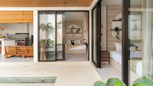 A modern hotel room with a sliding glass door leading to a balcony, a kitchen area, and a bedroom with a bed and nightstands. - Perenenan Home (Pererenan)
