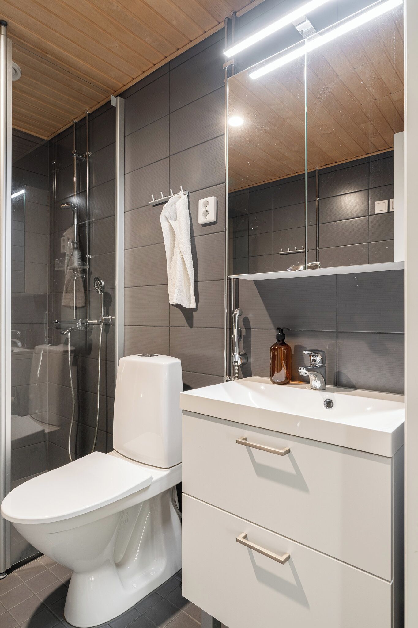 Een moderne badkamer met toilet, douche, wastafel en spiegel.