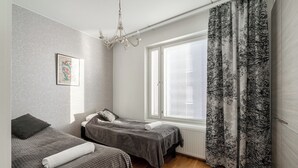 Ein Zimmer mit zwei Betten, einem Fenster mit Jalousien, einer Chandelier und einem gemusterten Vorhang.